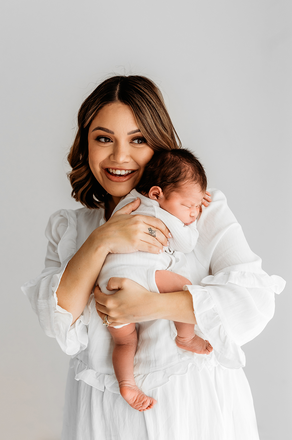 mum smiling holding baby showcasing dress for the what to wear to a newborn & baby photo shoot guide