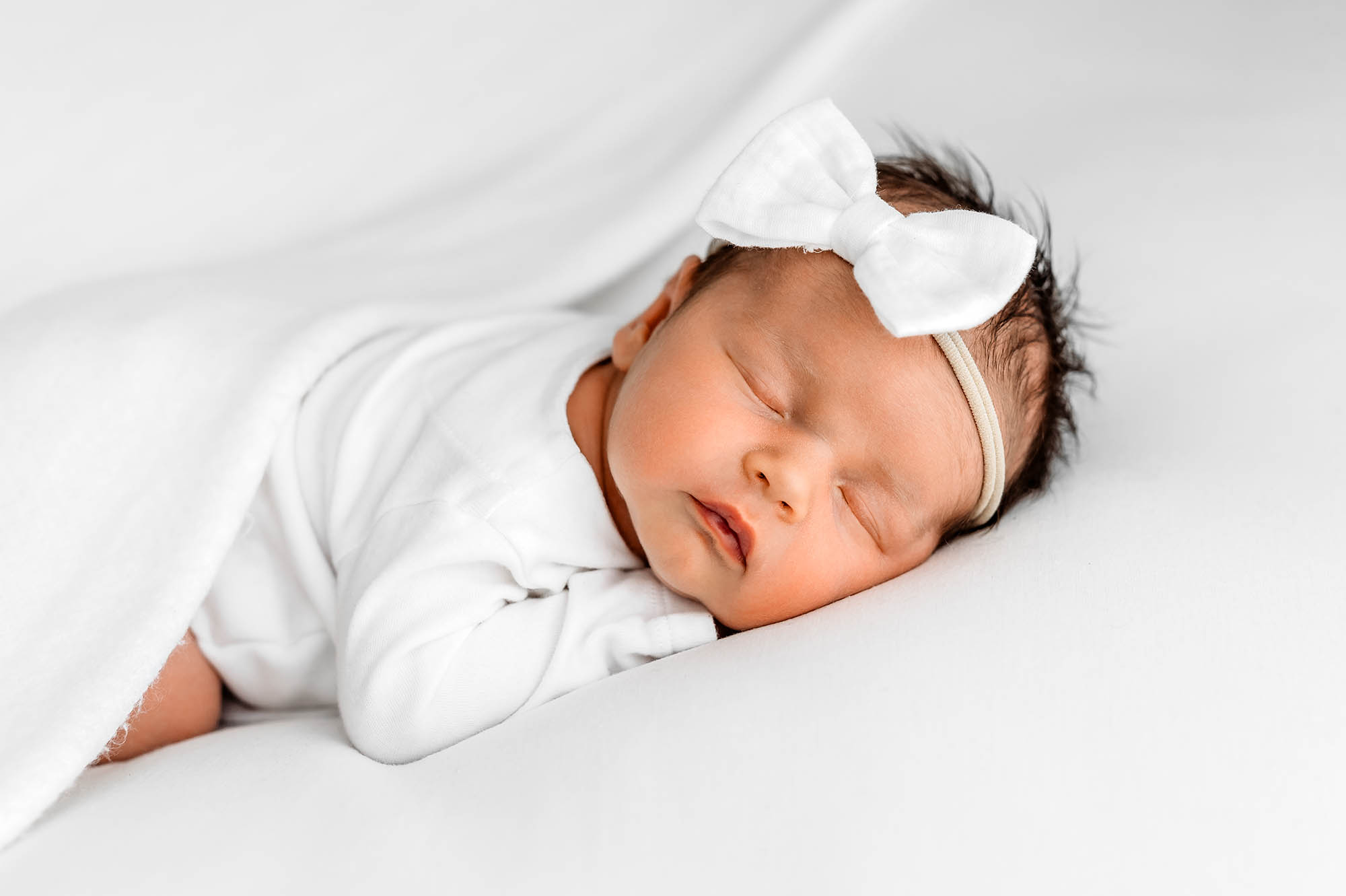 Baby in a bow laid on tummy with natural newborn photographer Barnsley